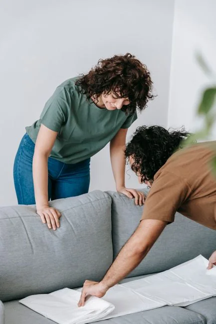 Une femme en pull gris nettoie une table avec soin, illustrant un entretien de la maison réalisé dans le confort.