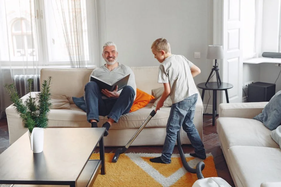 Vue rapprochée de personnes nettoyant un sol en bois avec un balai et une pelle à poussière à l'intérieur.